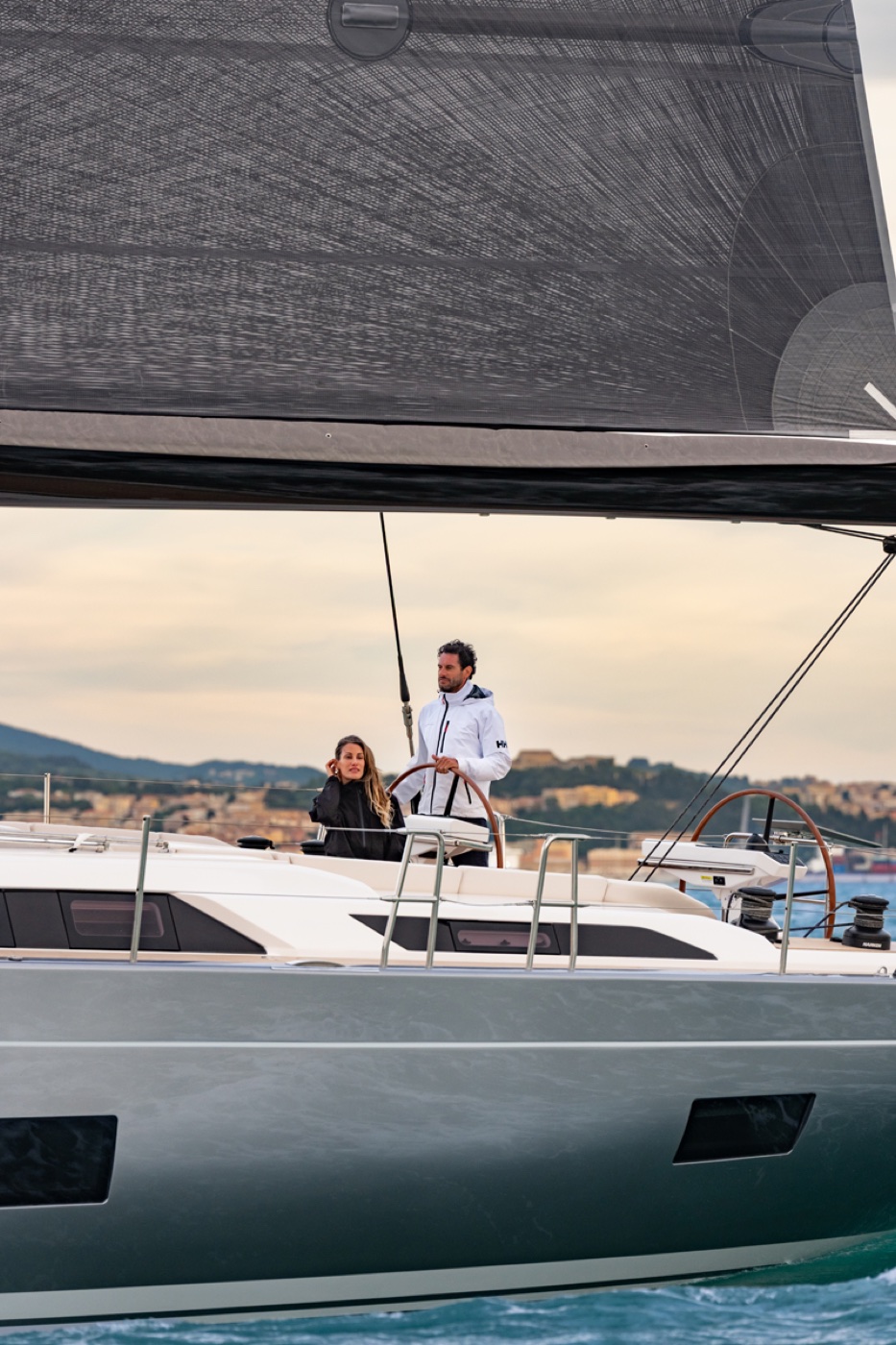 Una coppia al timone del Grand Soleil 60 durante la navigazione, con la costa sullo sfondo. Foto: Gianluca Napthalina Camporesi / Grand Soleil Yachts